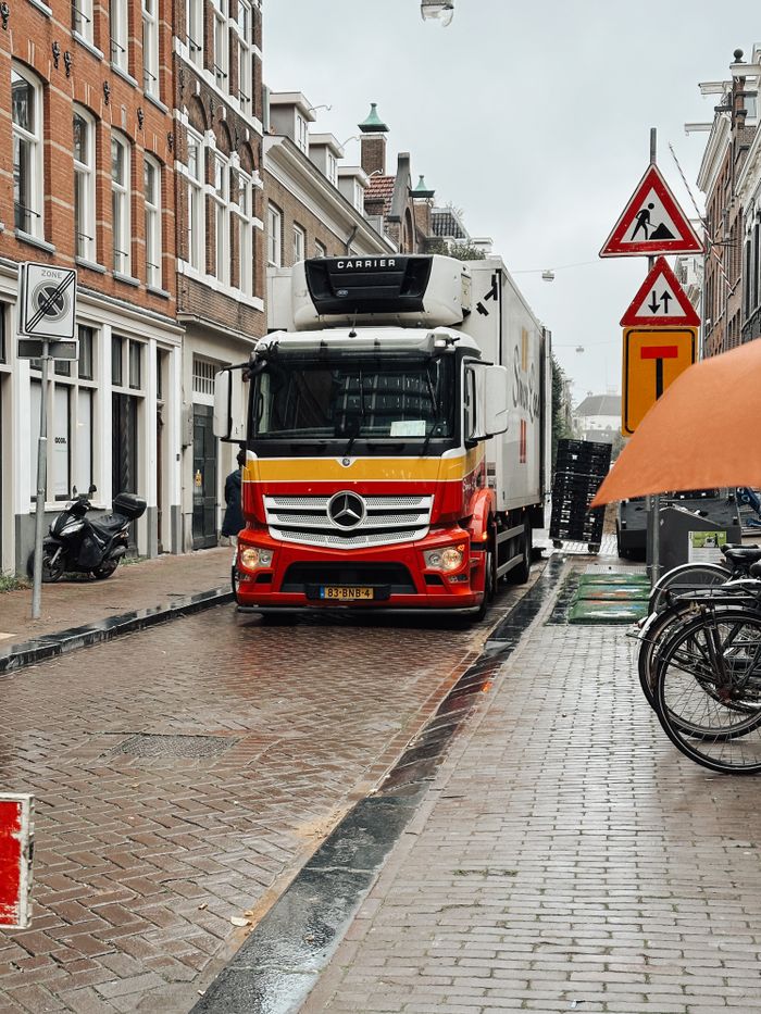 about-us A delivery truck navigates a narrow, wet street in Amsterdam on a rainy day.