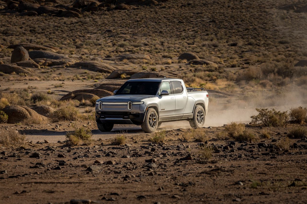 Electric pickup truck navigating a rocky desert landscape, showcasing off-road capability and rugged terrain.