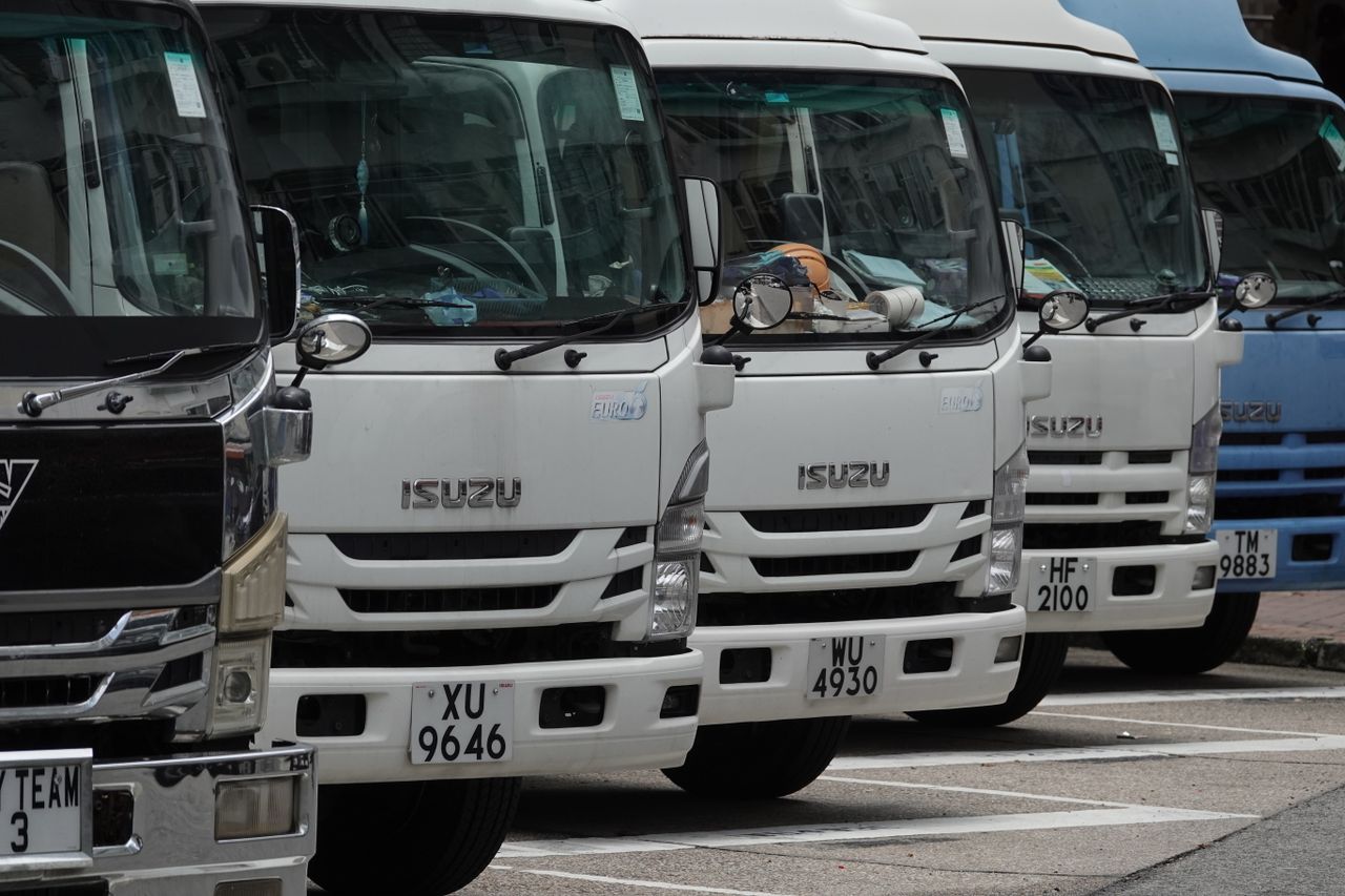 our-story Parked Isuzu trucks lined up in the city, ready for delivery. Ideal for transport and logistics themes.